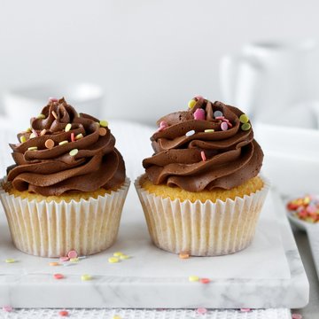 Schoko-Cupcakes angerichtet auf einem Brett mit bunten Streuseln